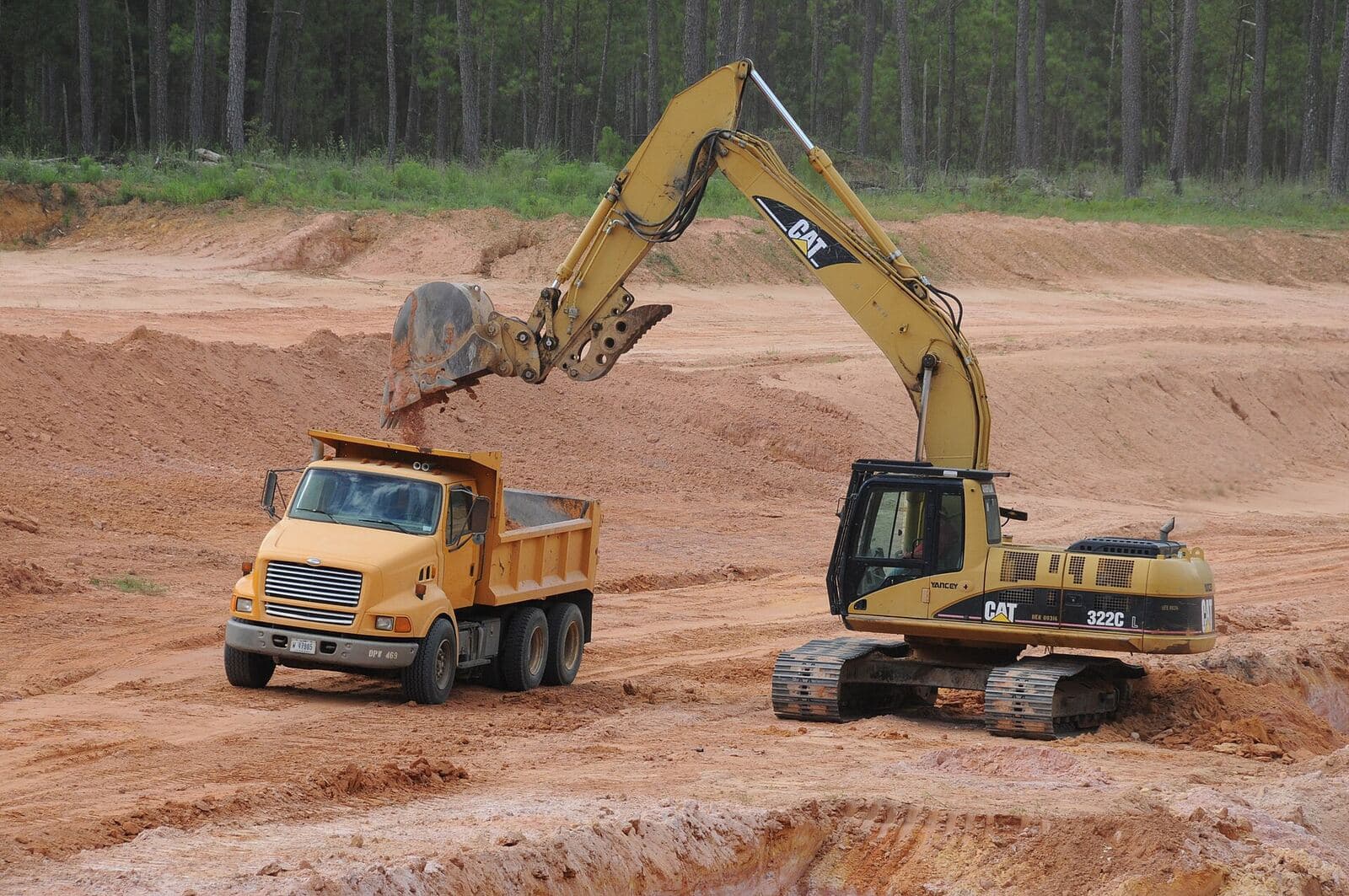 An excavator loading a dump truck on open ground cut down to subsoil.