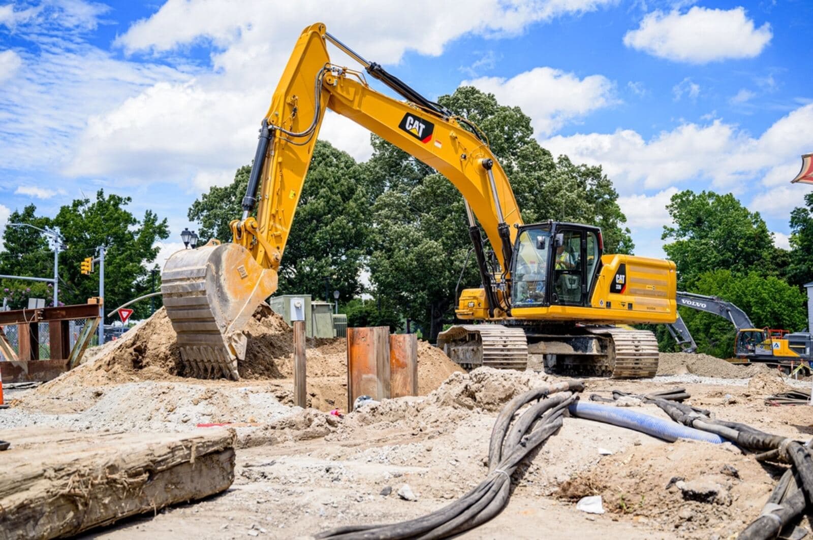 An excavator with its bucket lowered beside a pile of excavated soil on an open site.